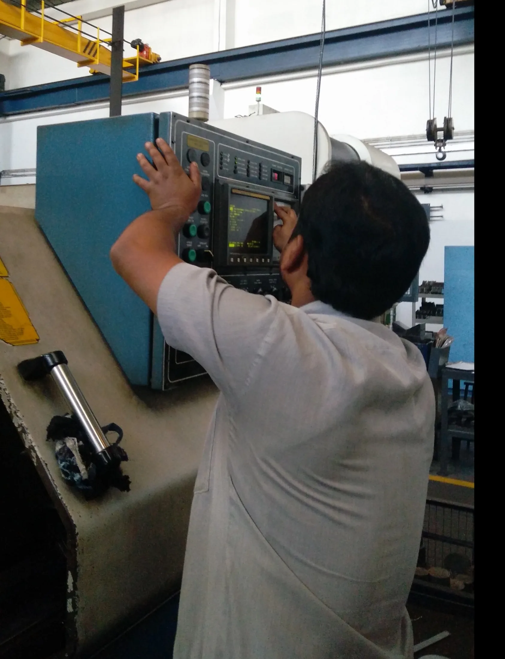 Operator reaching upward with both arms to use a high-mounted CNC control panel.