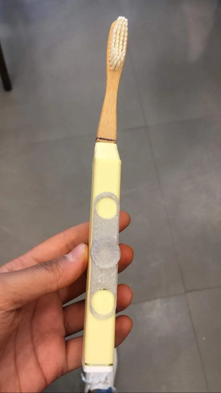Hand holding an assembled translucent and yellow toothbrush prototype.